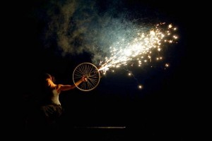 a woman holds a bike wheel shooting a sparkly, gerb firework effect