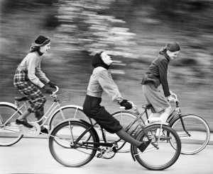 A black & white image of 3 young women speeding along a road on their bikes