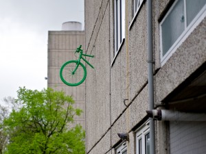 the front wheel and handlebars of a bright green bike emerge from the wall of a block of flats in Roehampton
