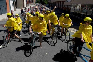 Cyclists stretch down the road in Bristol's CarniVelo ride, fronted by a group on tandems wearning yellow helmets, macs and goggles waving their arms in the air