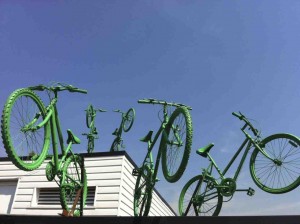 Five green painted bikes, leap from the two roof levels of Putney Leisure Centre